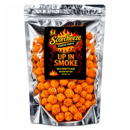 A silver stand-up pouch of Scorchzee Cheese Puffs, featuring a prominent black label with fiery orange and yellow graphics and the text 'UP IN SMOKE'. The clear front of the bag shows numerous round, orange-brown cheese puffs seasoned with specks of seasoning.